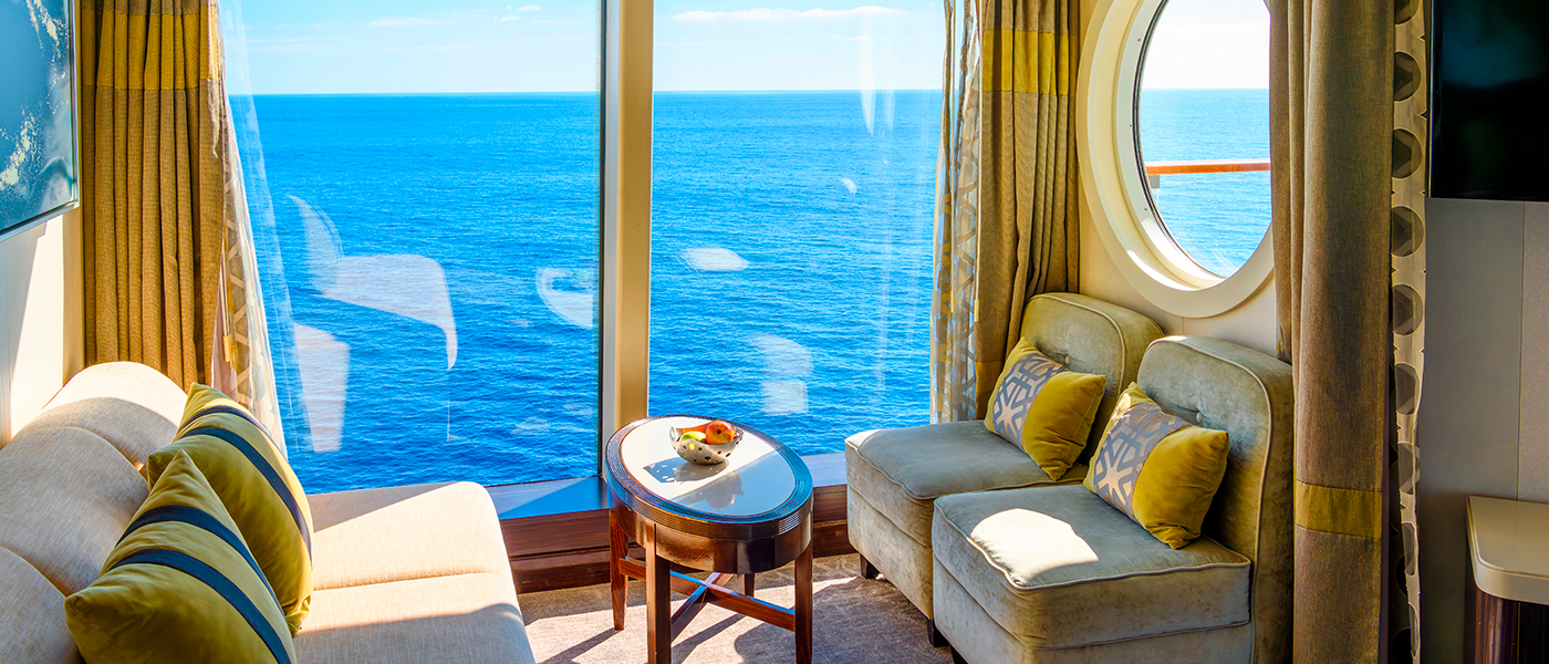Helle Sitzkombination mit Sofa und Sessel am Fenster eines Kreuzfahrtschiffes mit Blick auf das Meer.